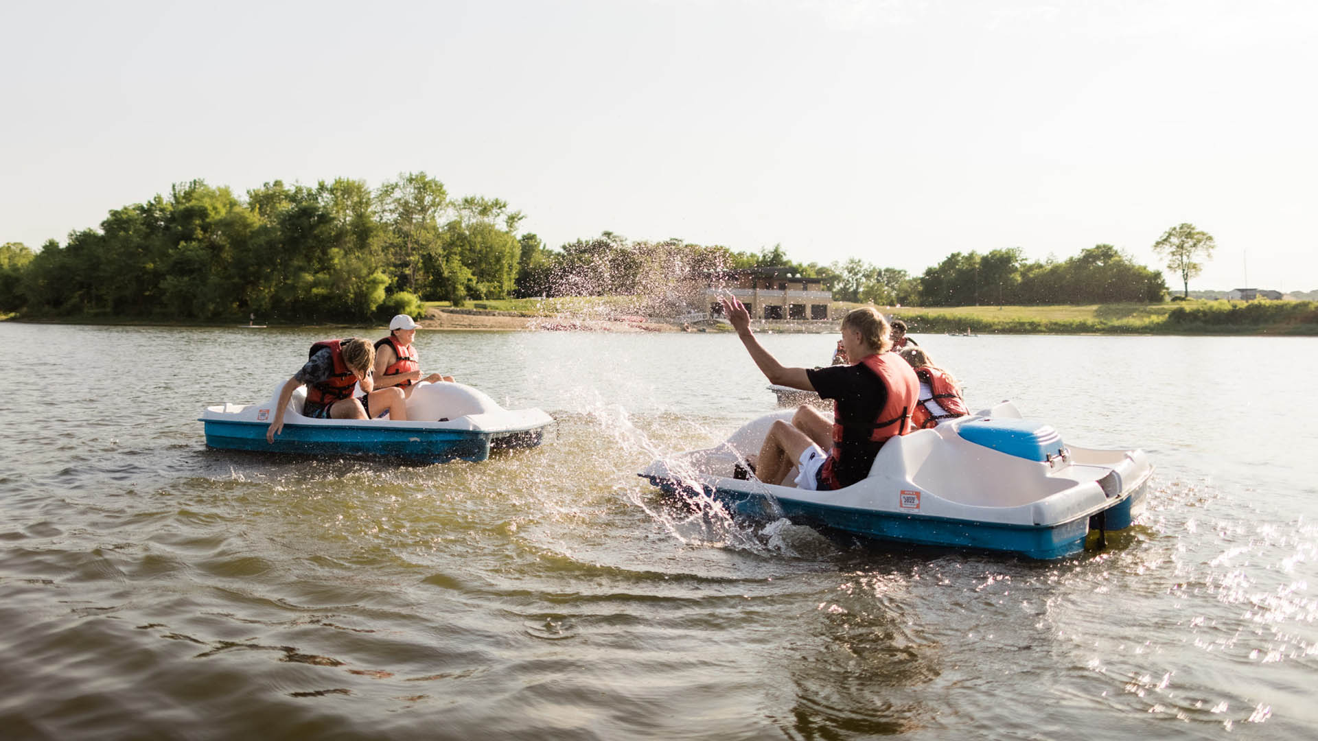 A group of young people in peddle boats splashing each other