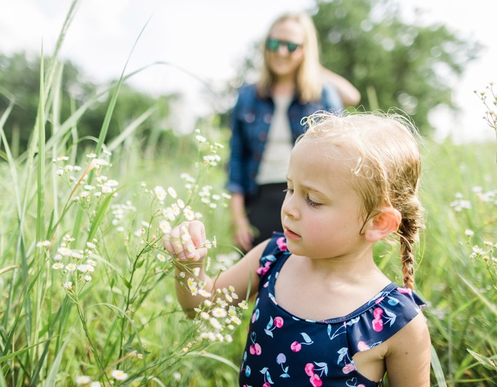 A young girl looking at white flowers in a prairie
