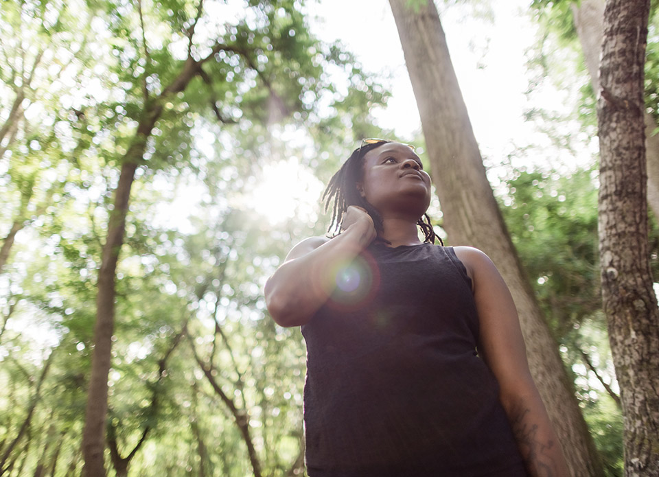 Woman standing in the woods with the sun shining through leaves above her