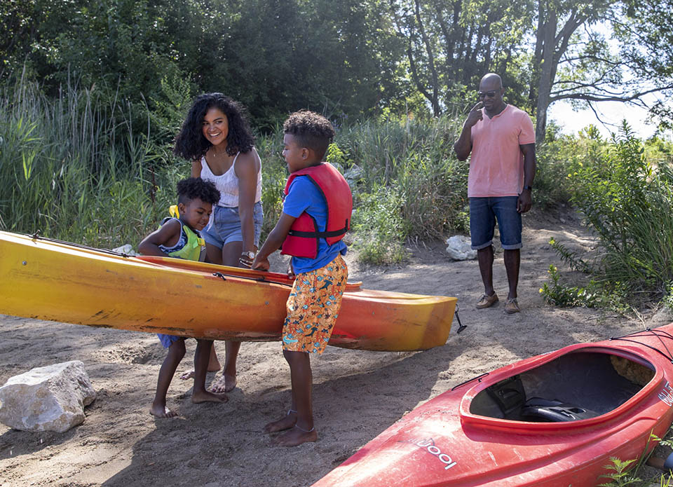 A mom helping her two young sons carry a kayak to the water
