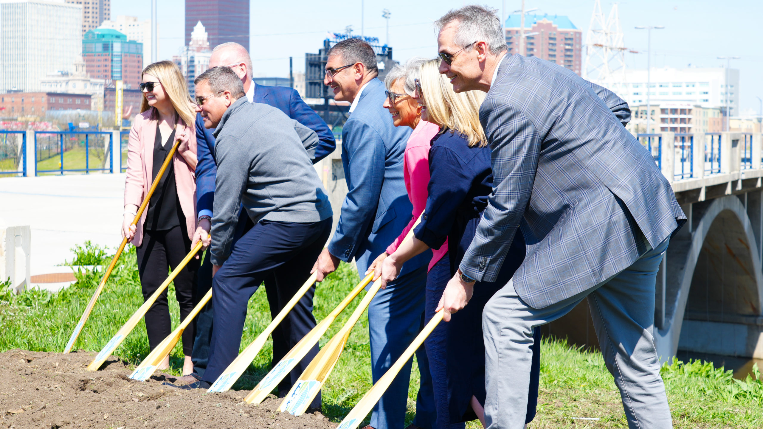 A group of well dressed people using ICON oars to dig in to a pile of dirt at the ground breaking ceremony