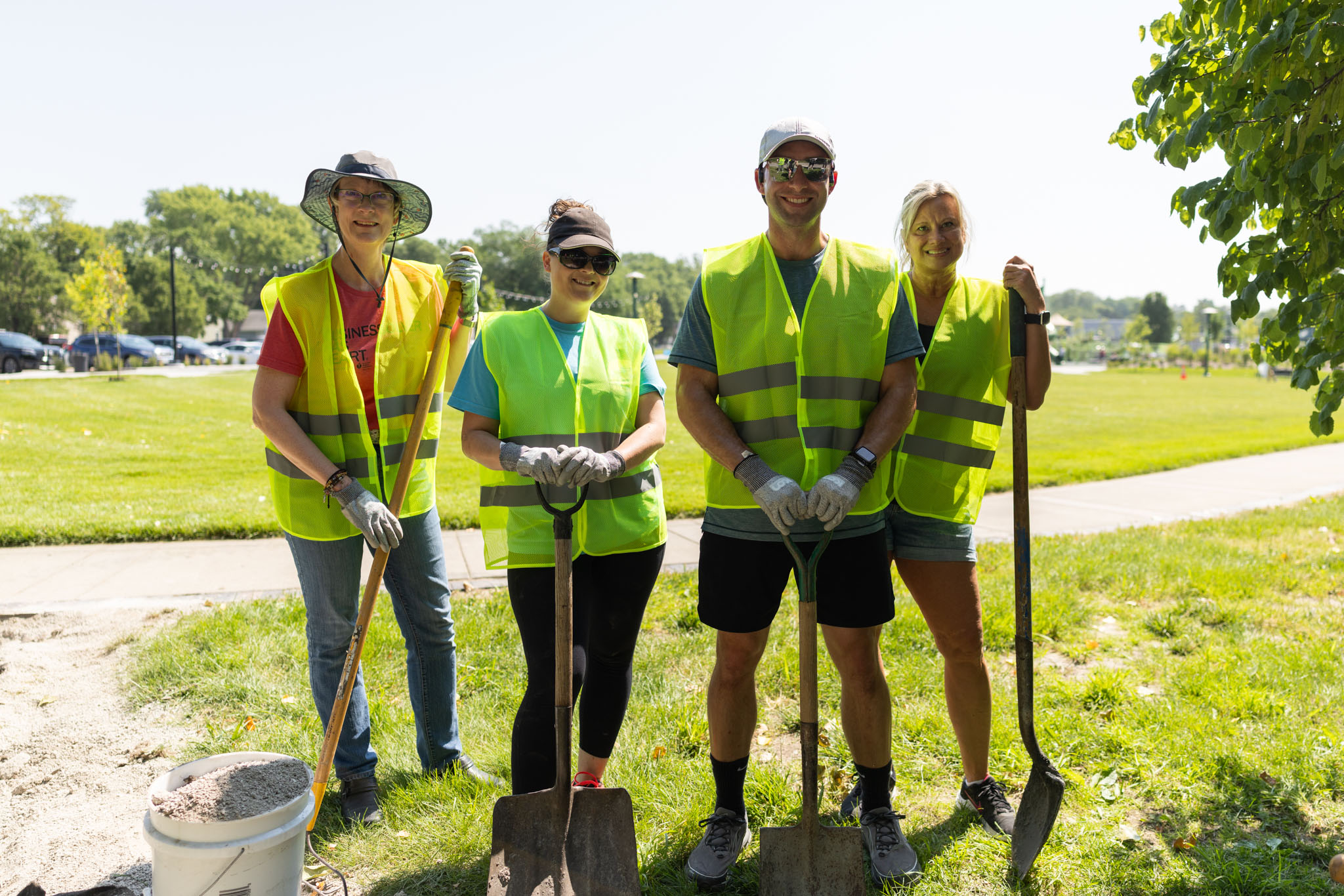 Four volunteers wearing yellow hi-vis vests and holding shovels