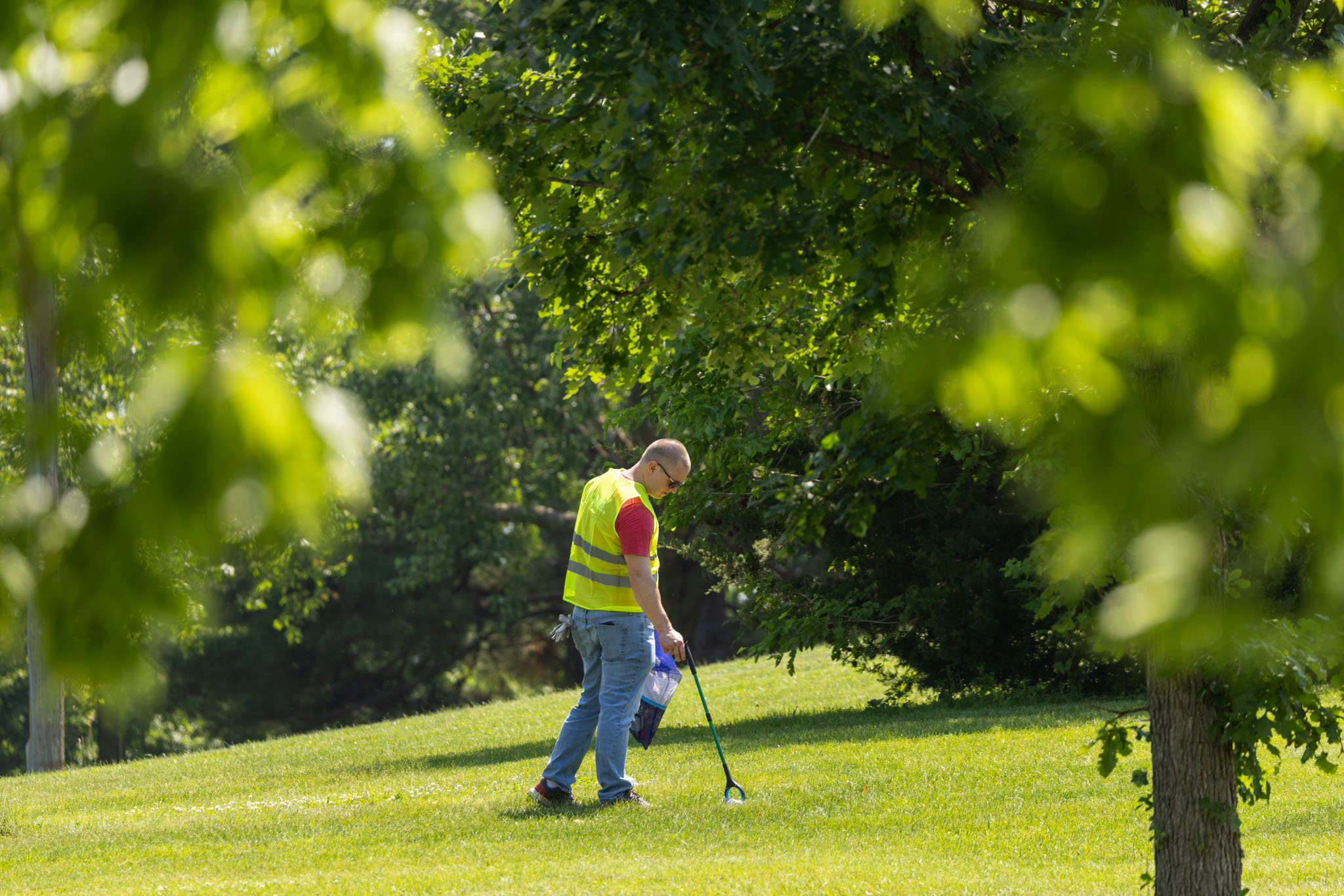 A man in a yellow vest picking up a piece of trash