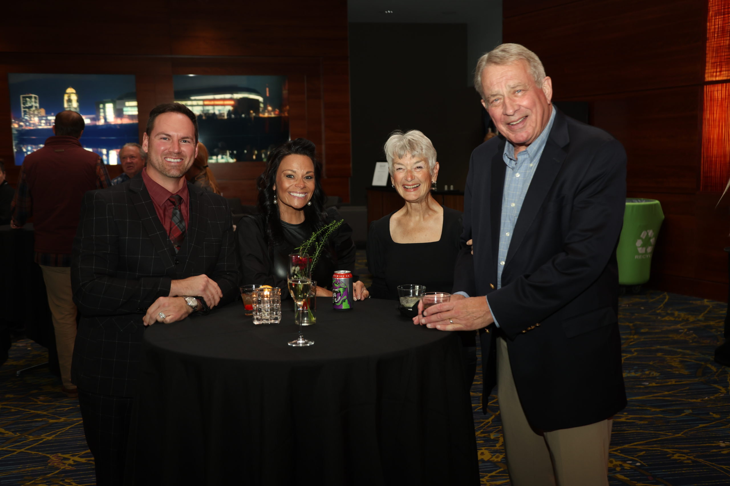 A group of four people standing at a cocktail table with their drinks and smiling at the camera