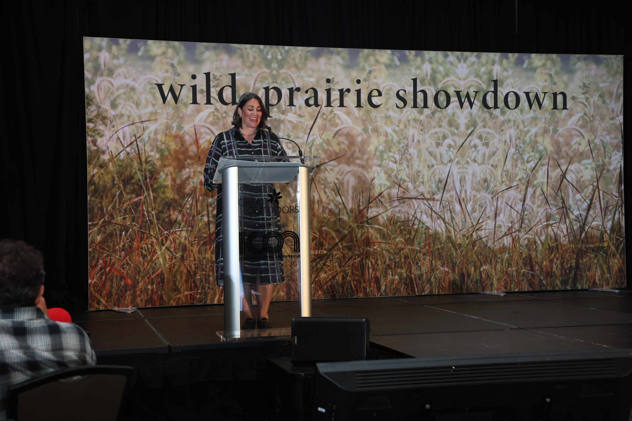 A woman in a black and white dress smiling and speaking in to a microphone