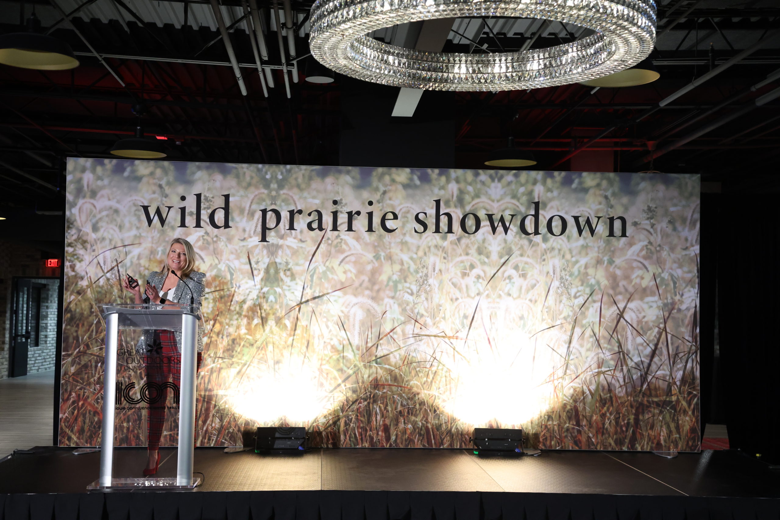A presenter on stage in a glittery jackets and speaking in to the microphone