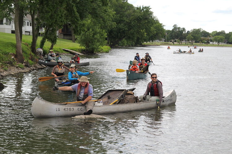 A few different groups of canoers pulling up by the shore with large pieces of metal in their canoes