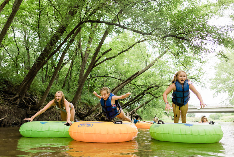 A group of kids jumping on to their tubes in the creek