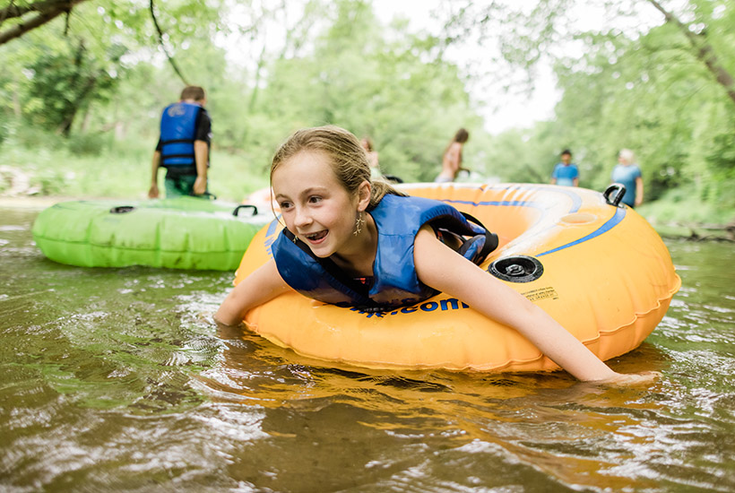 A young girl floating on her stomach on a tube down Beaver Creek and smiling