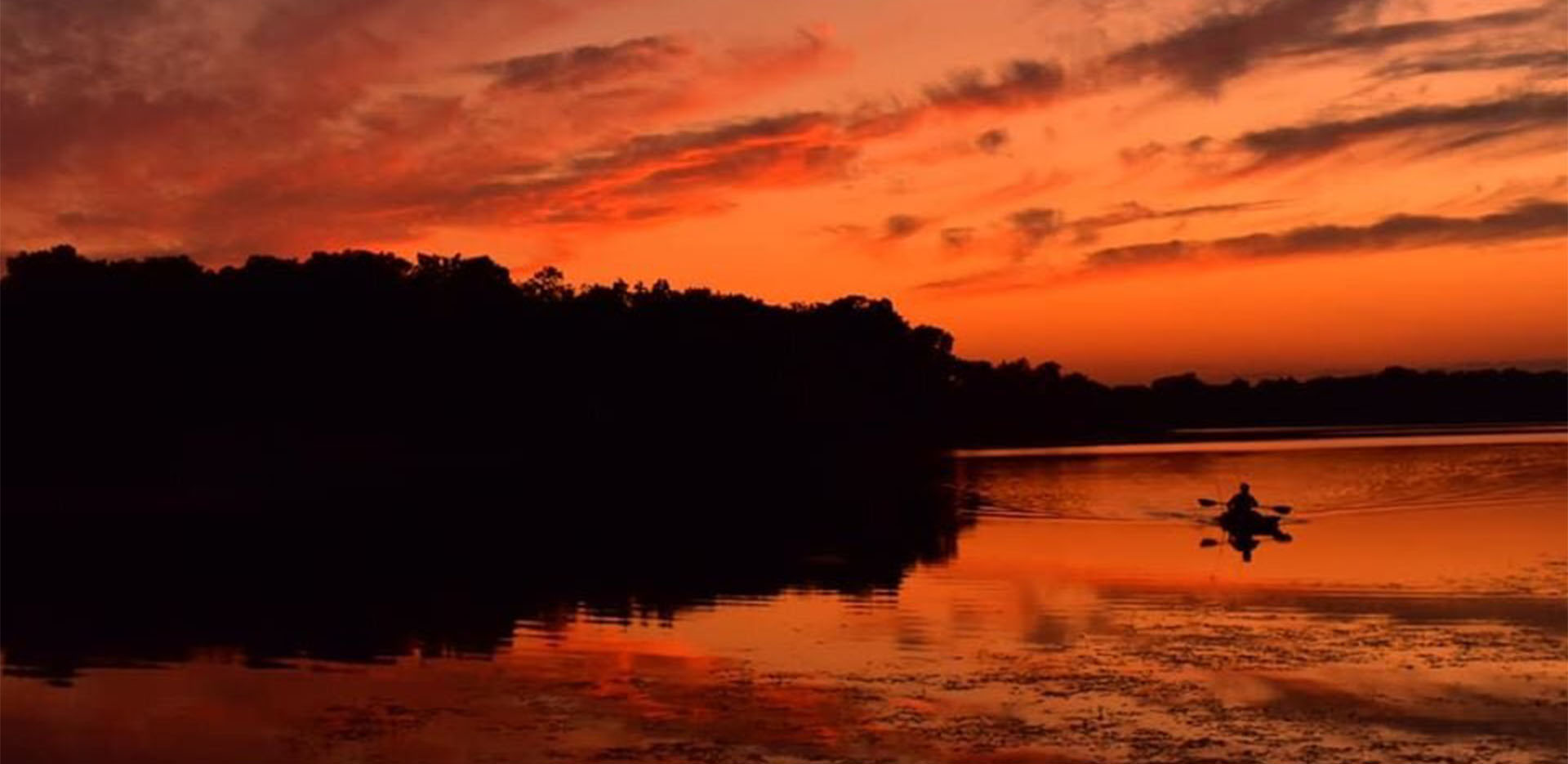 Silhouette of a kayaker out on a river during a beautiful orange sunset