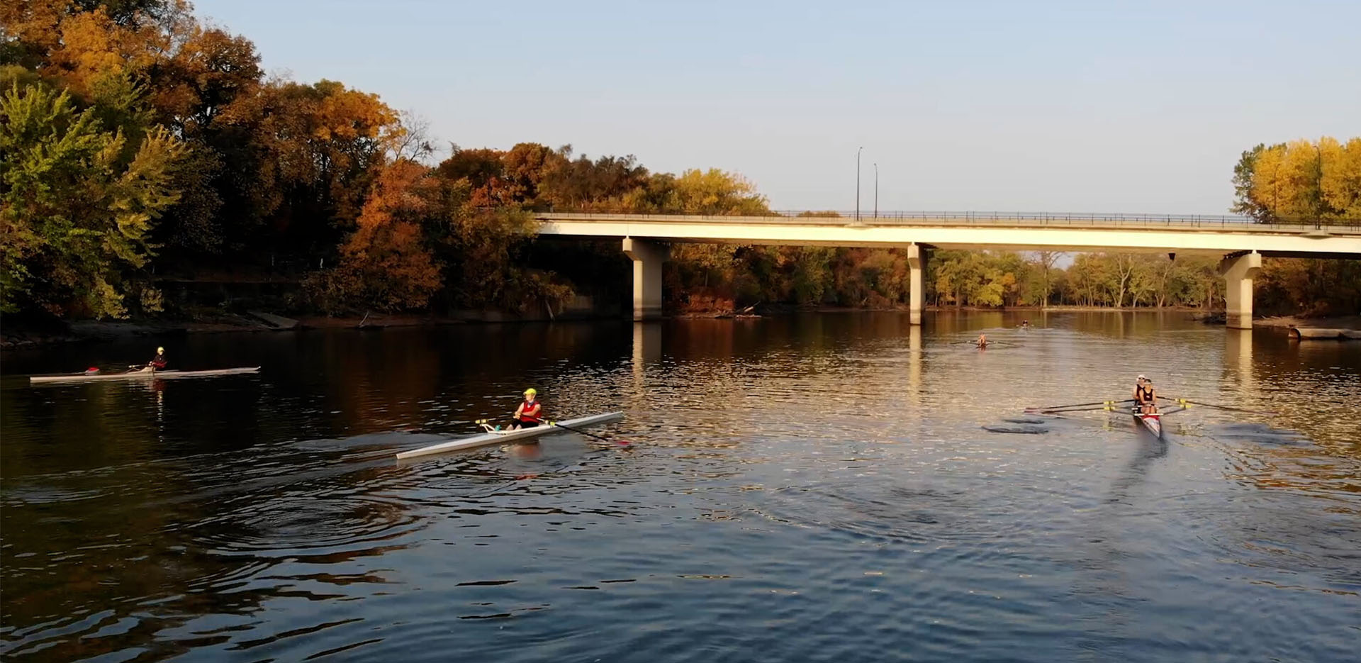 A group of rowers going under a bridge on the Des Moines River