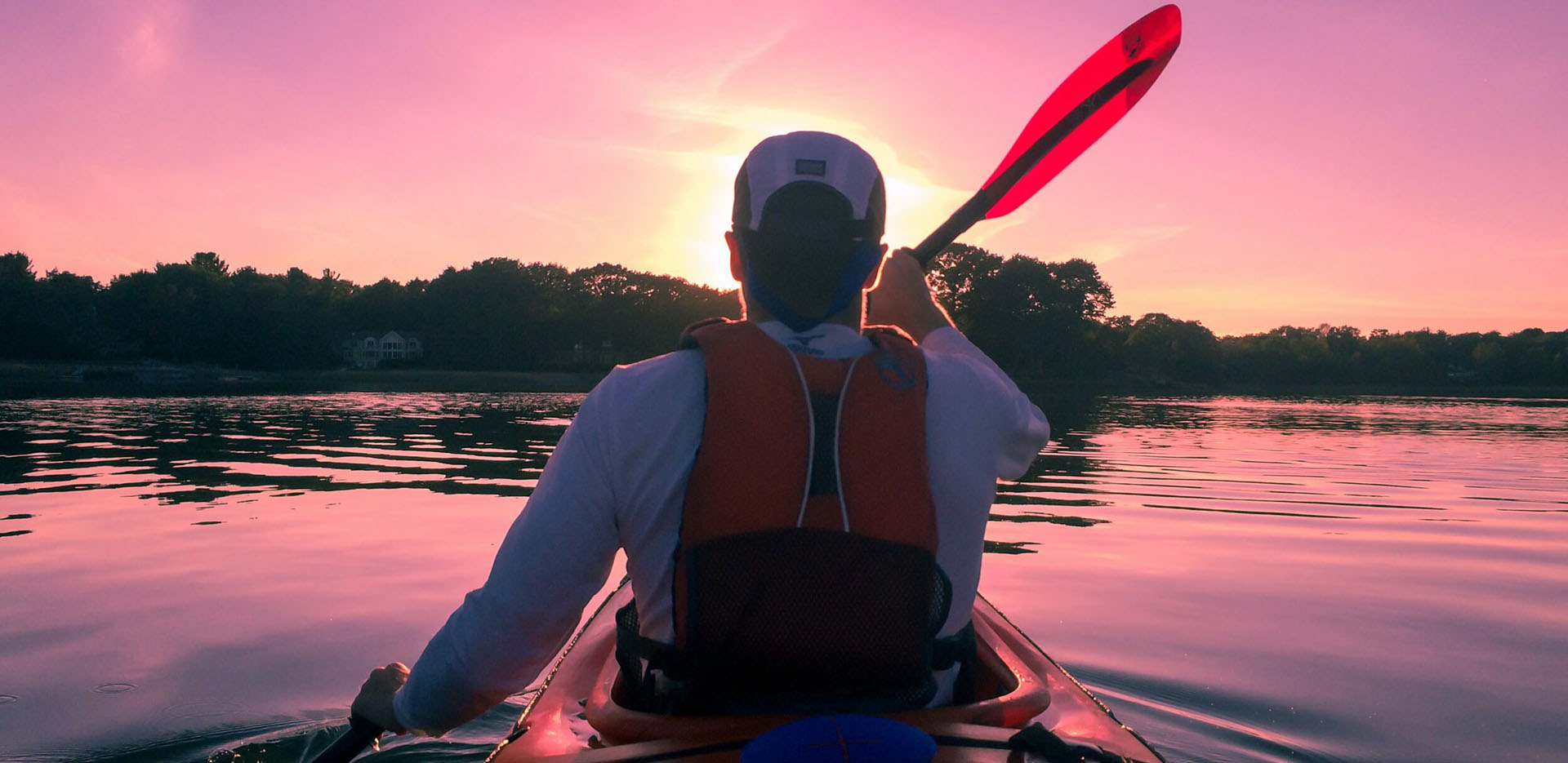 A person seen from behind is paddling a kayak at sunset