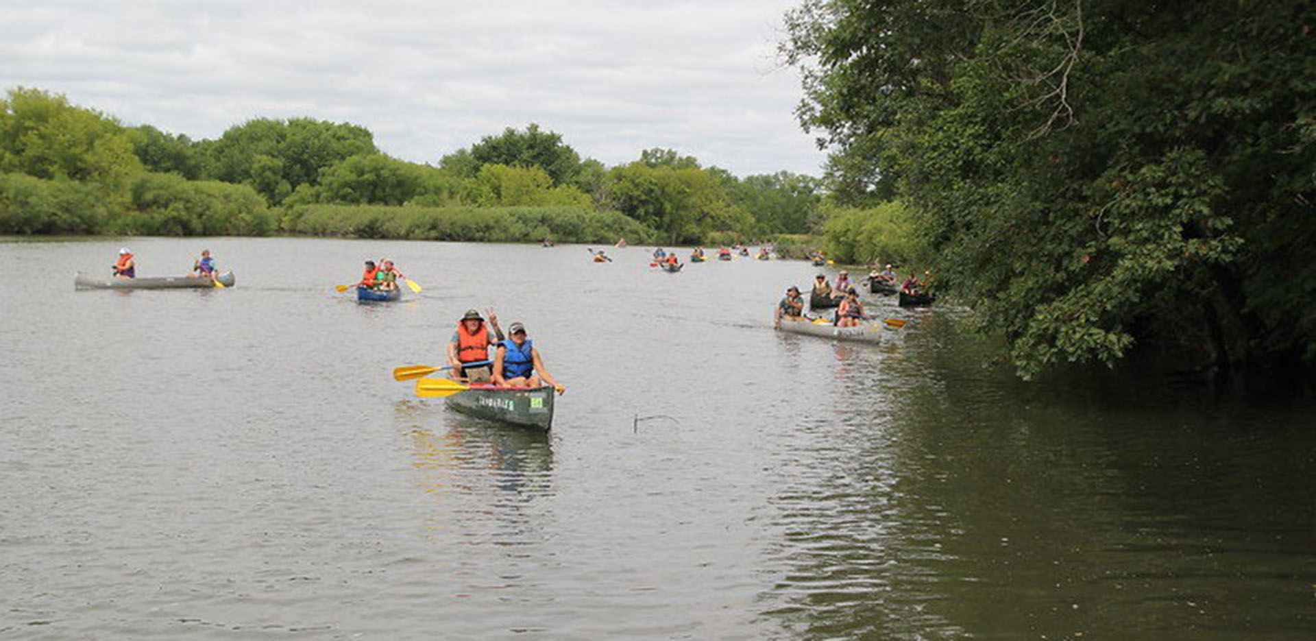 A large group of people in canoes padding the river on clean up day
