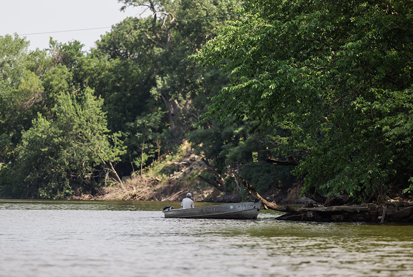 The back of a man fishing from a metal fishing boat on the Des Moines River