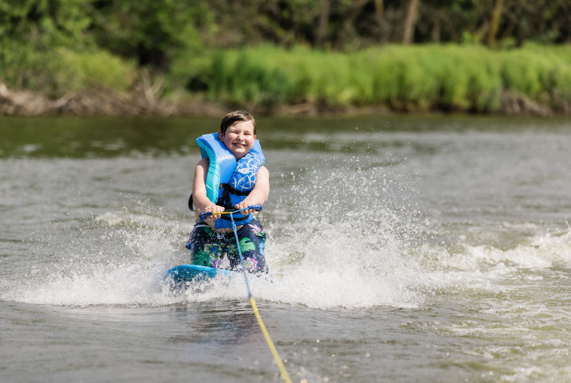 A boy with a big smile kneeboarding while being towed behind a boat