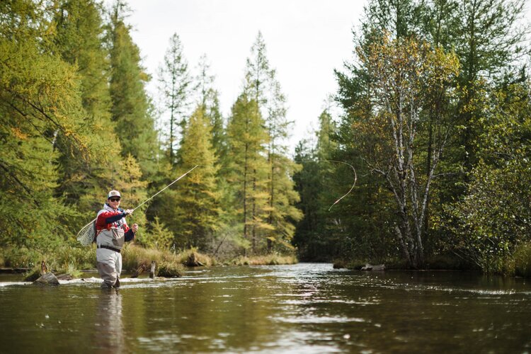 A man in waders standing in the middle of a river casting his fly fishing