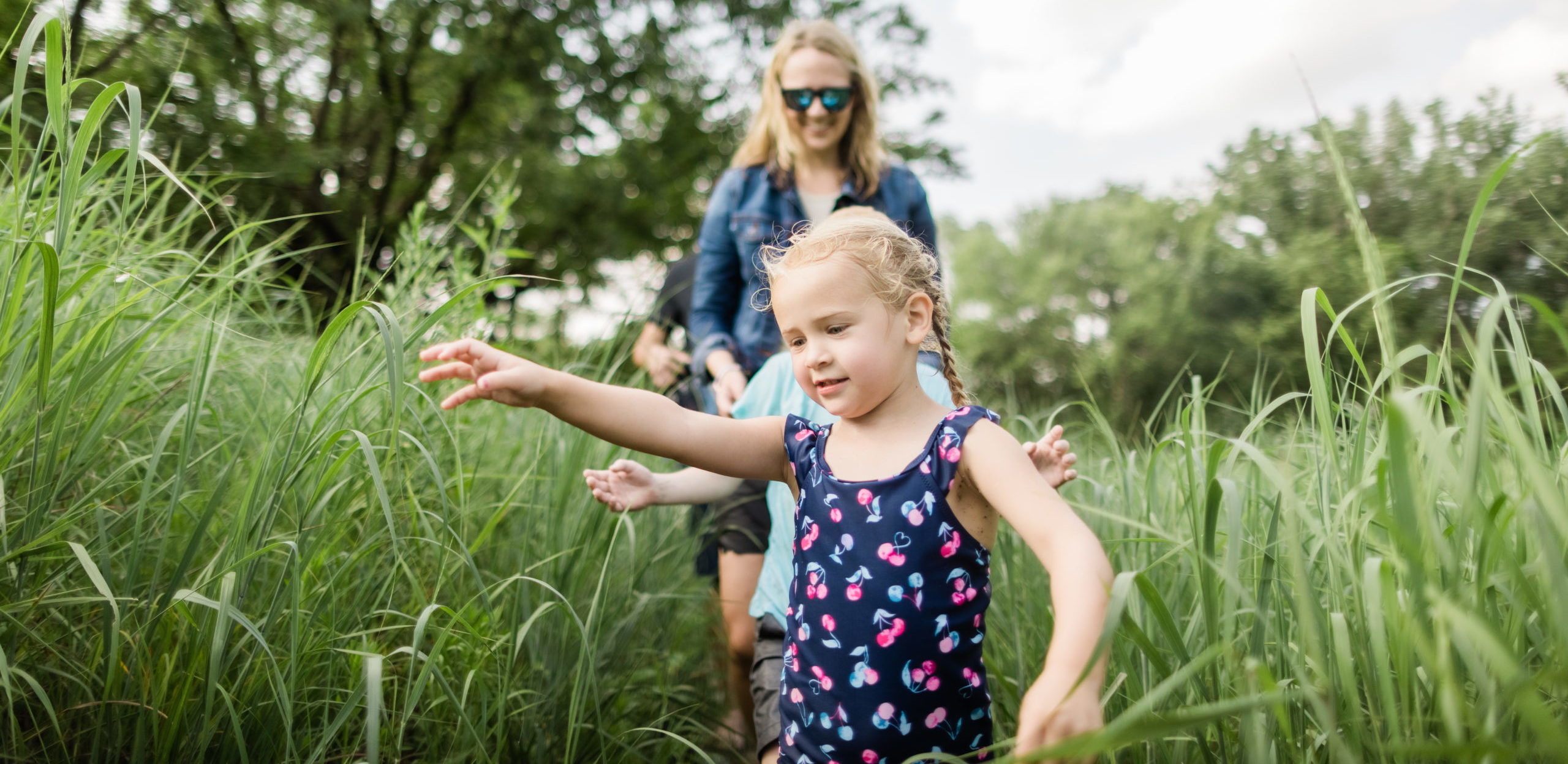 Family walking through tall grass along a single track trail