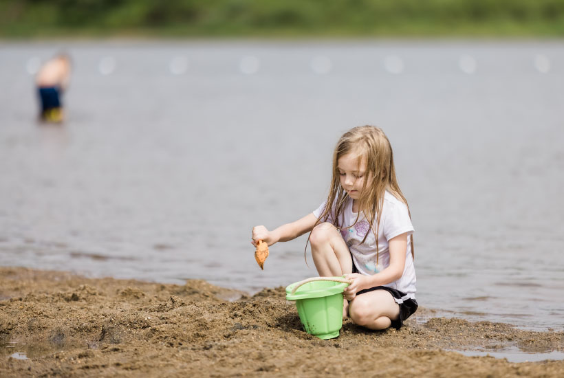 A little girl playing in the sand with a shovel and bucket