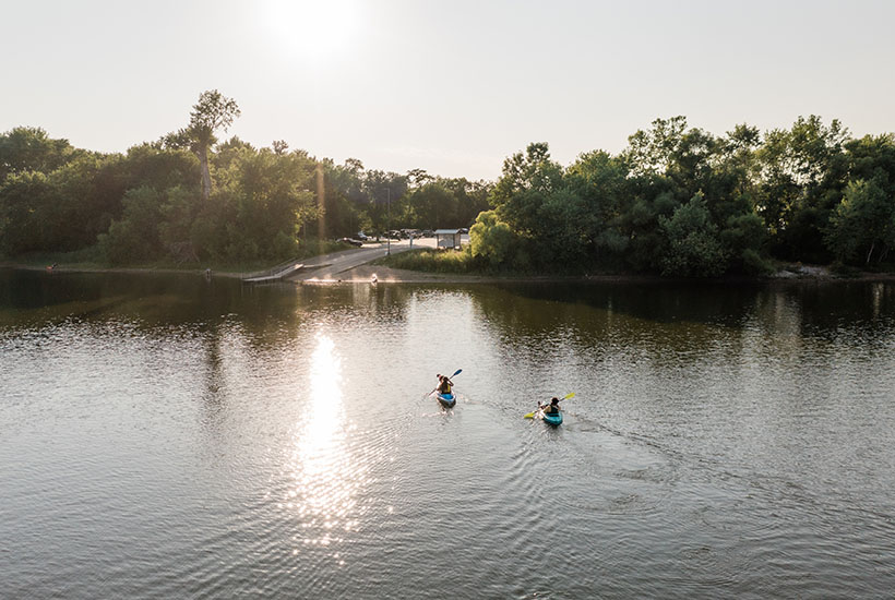 Two people kayaking towards a boat launch along the edge of the river.