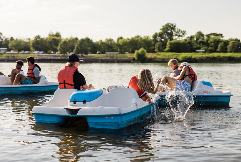 A group of teenagers splashing each other in pedal boats