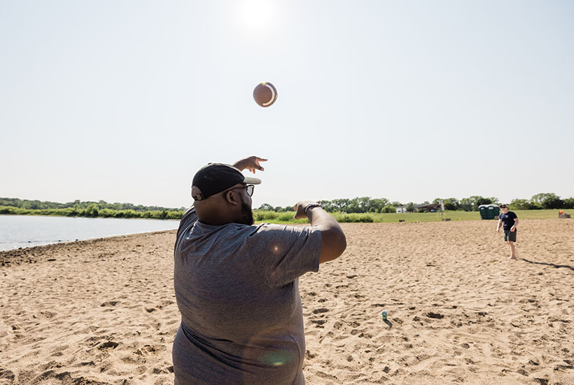 A man throwing a football to another person further down the beach