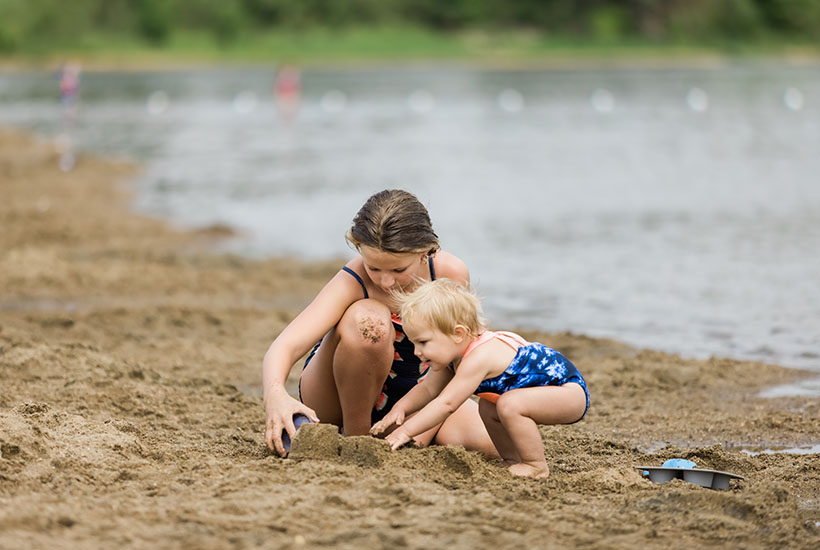 A young girl playing with a toddler in the sand