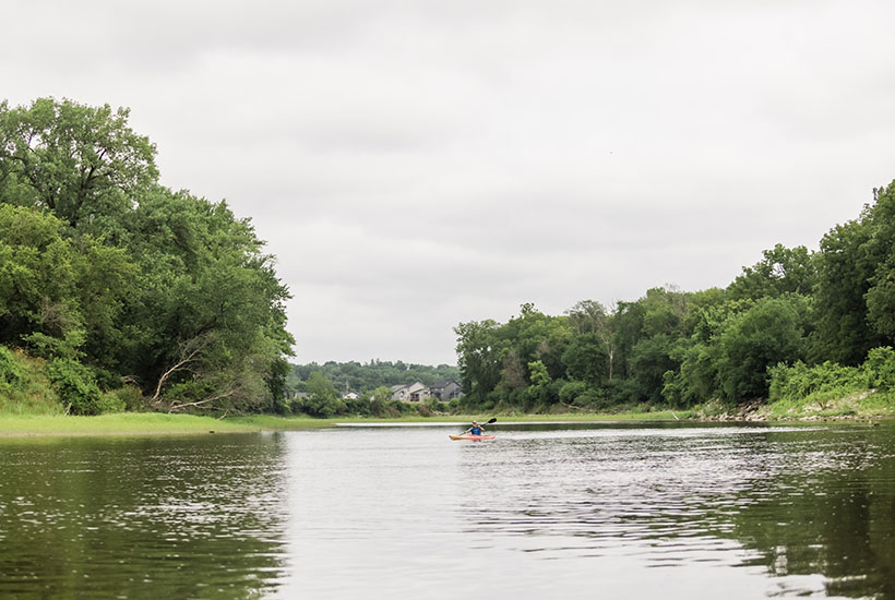 A kayaker padding on the tree lined Raccoon River