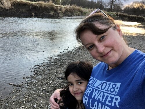 A woman in a blue shirt and a girl in a dark colored shirt taking a selfie next to the river