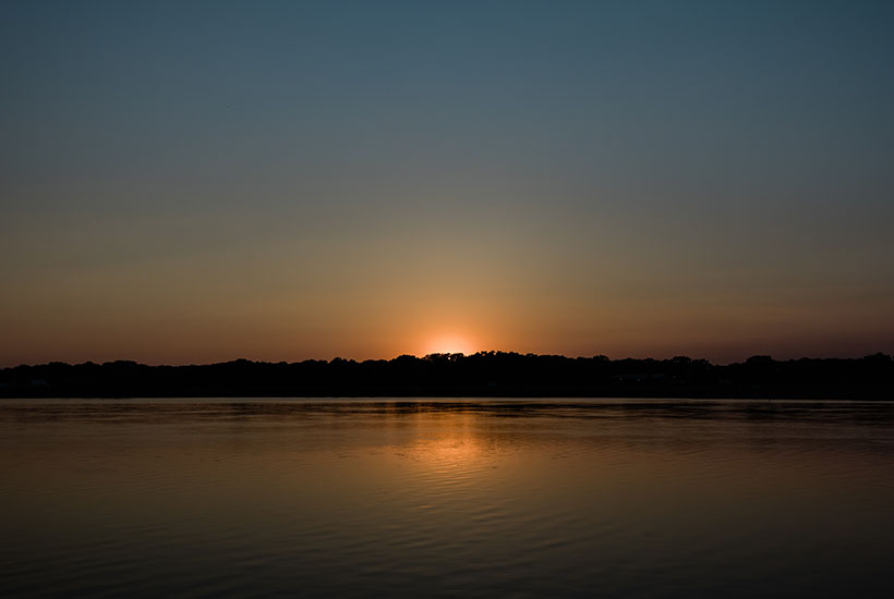 The end of a sunset over a body of water - there's still a slight glow from the sun over the trees and reflected in the water