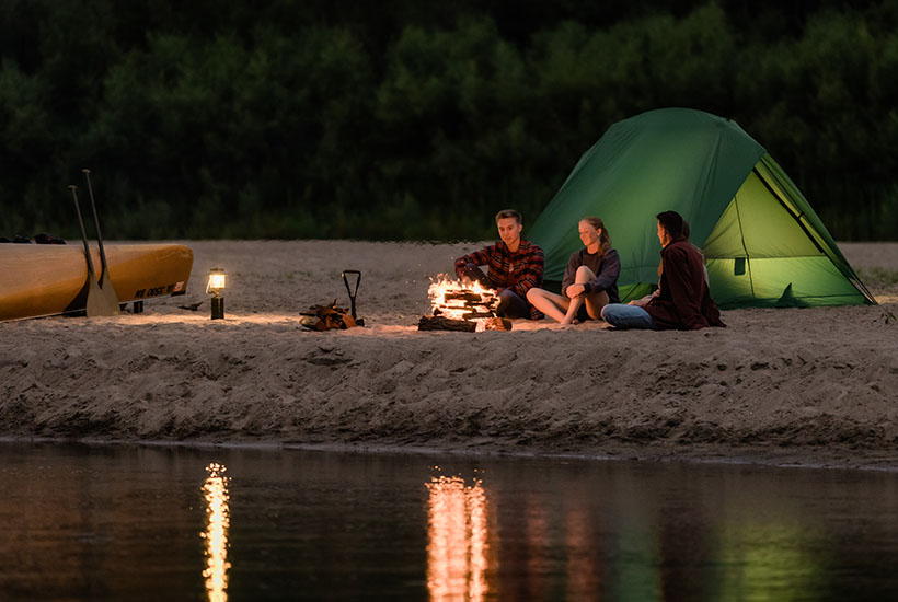 A camp set up on a sandbar with a small group of people sitting by the fire.