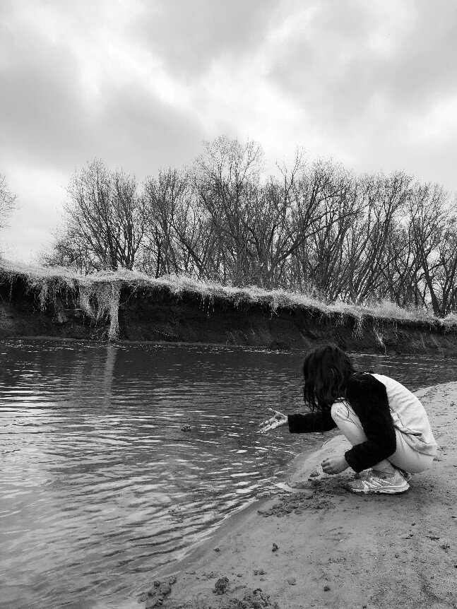 Black and white photo of a girl crouched down next to the water